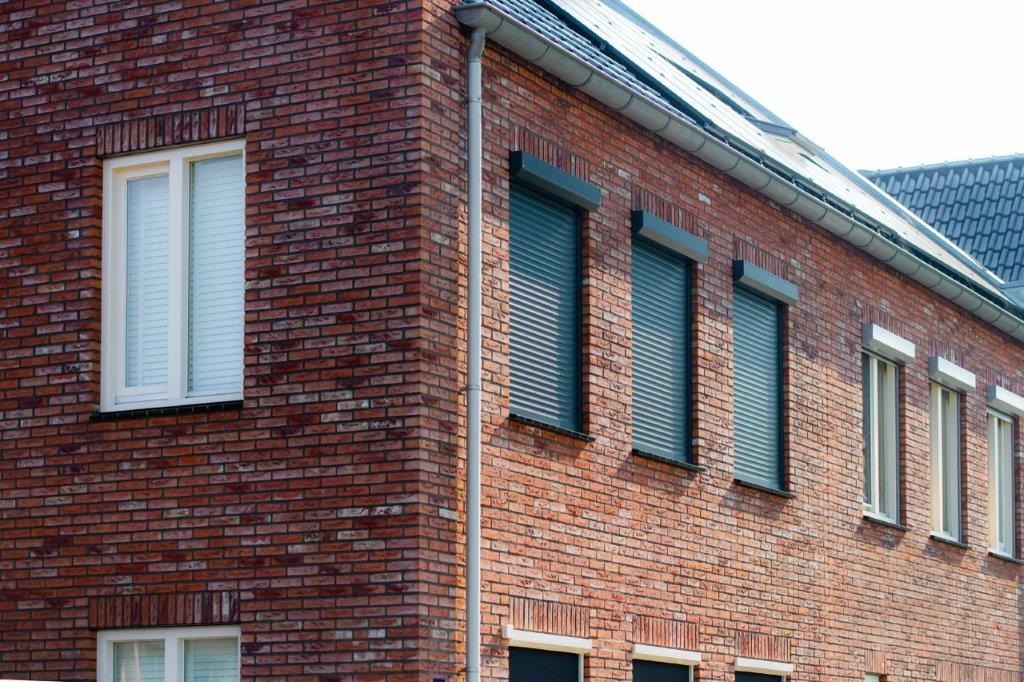 Donkere rolluiken voor de ramen van een bakstenen woning
