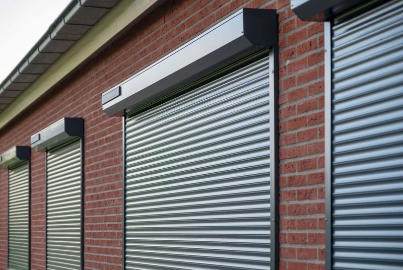 Grijze rolluiken met rolluikkasten voor de ramen van een bakstenen woning